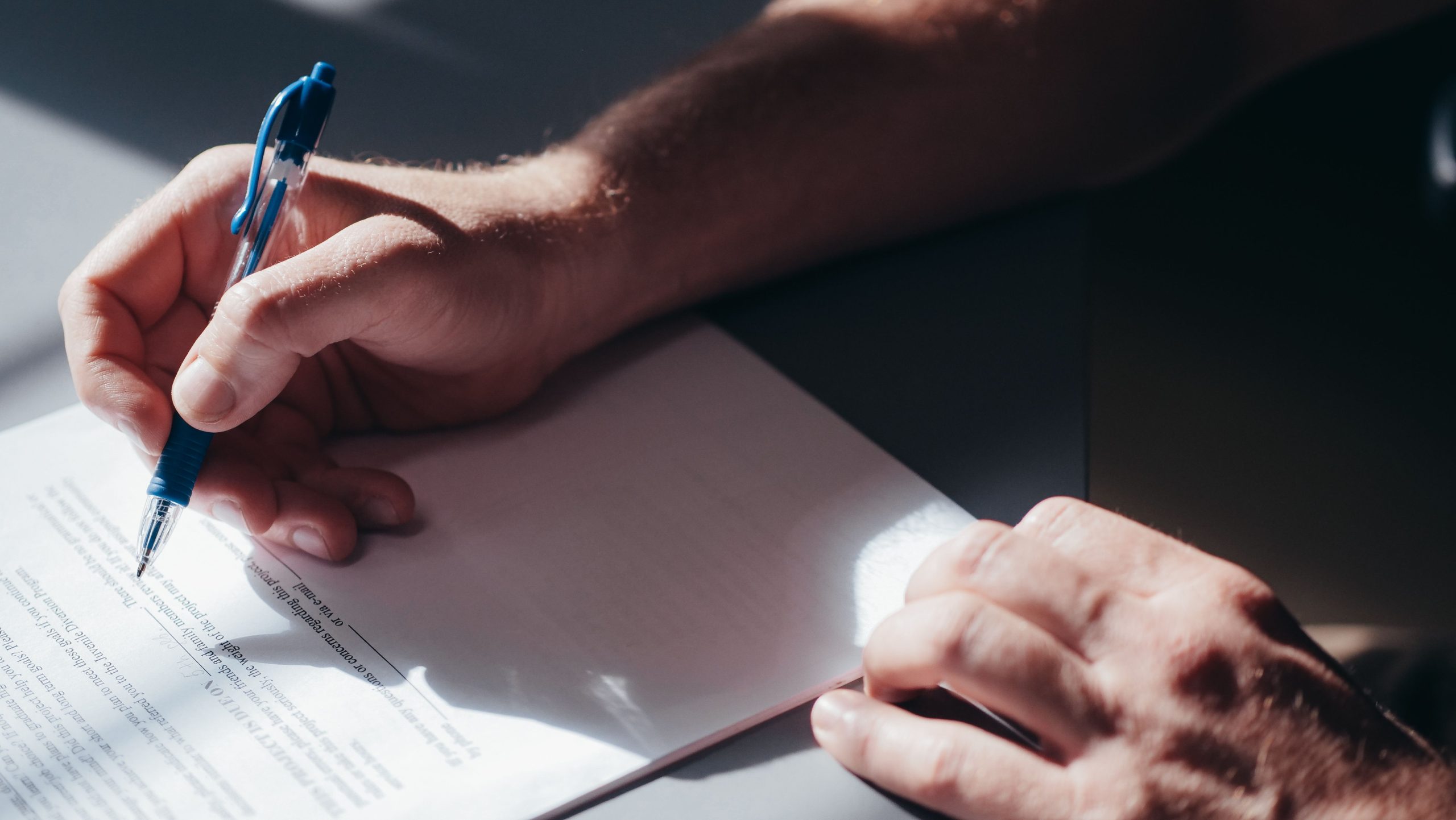 Main signant un document avec un stylo bleu